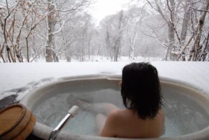 a young japanese woman in an open air bath while snowing